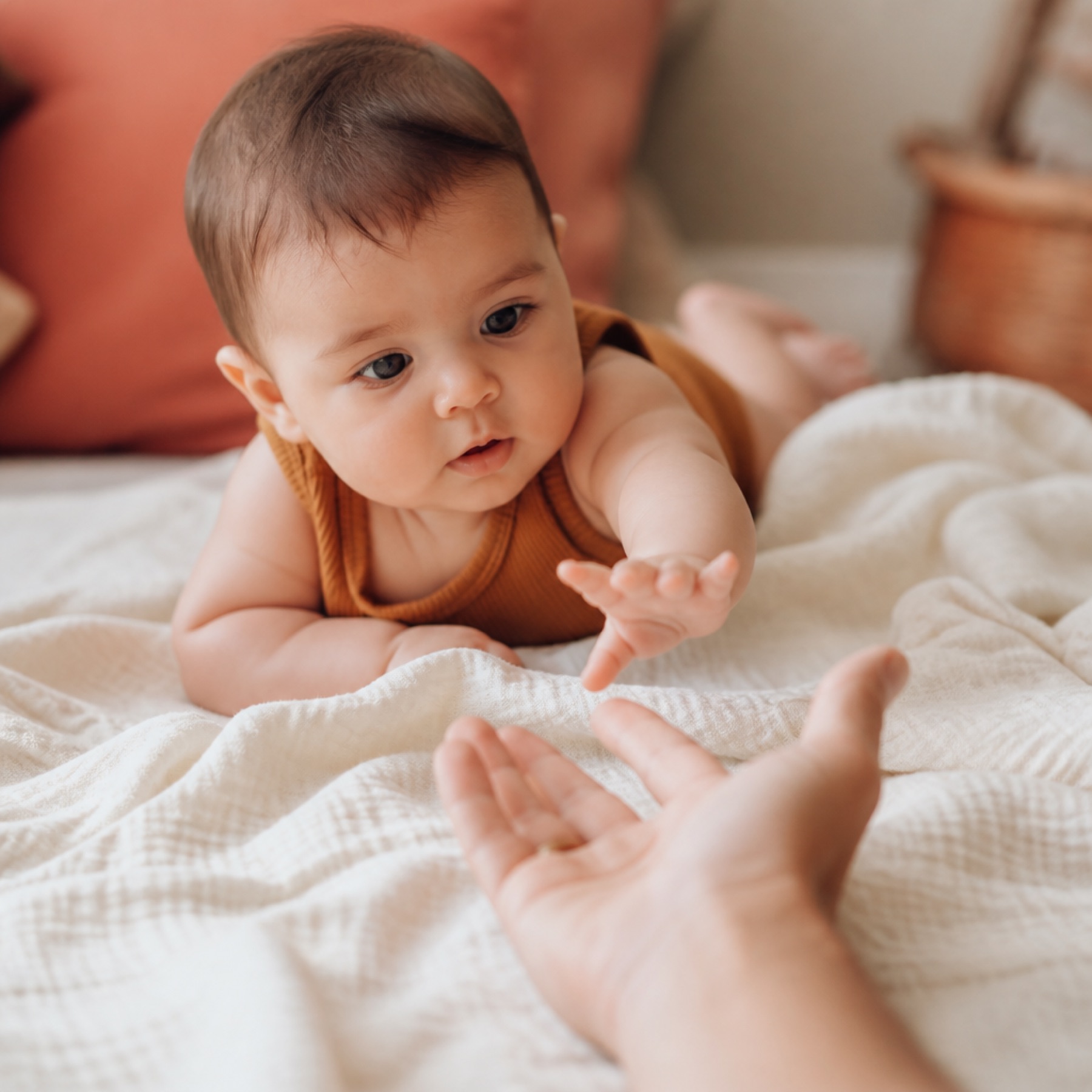 An infant reaching toward a parent’s hand on a cream blanket